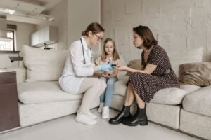 Clinician with a young girl and her mother on the sofa at home, NDIS high intensity support
