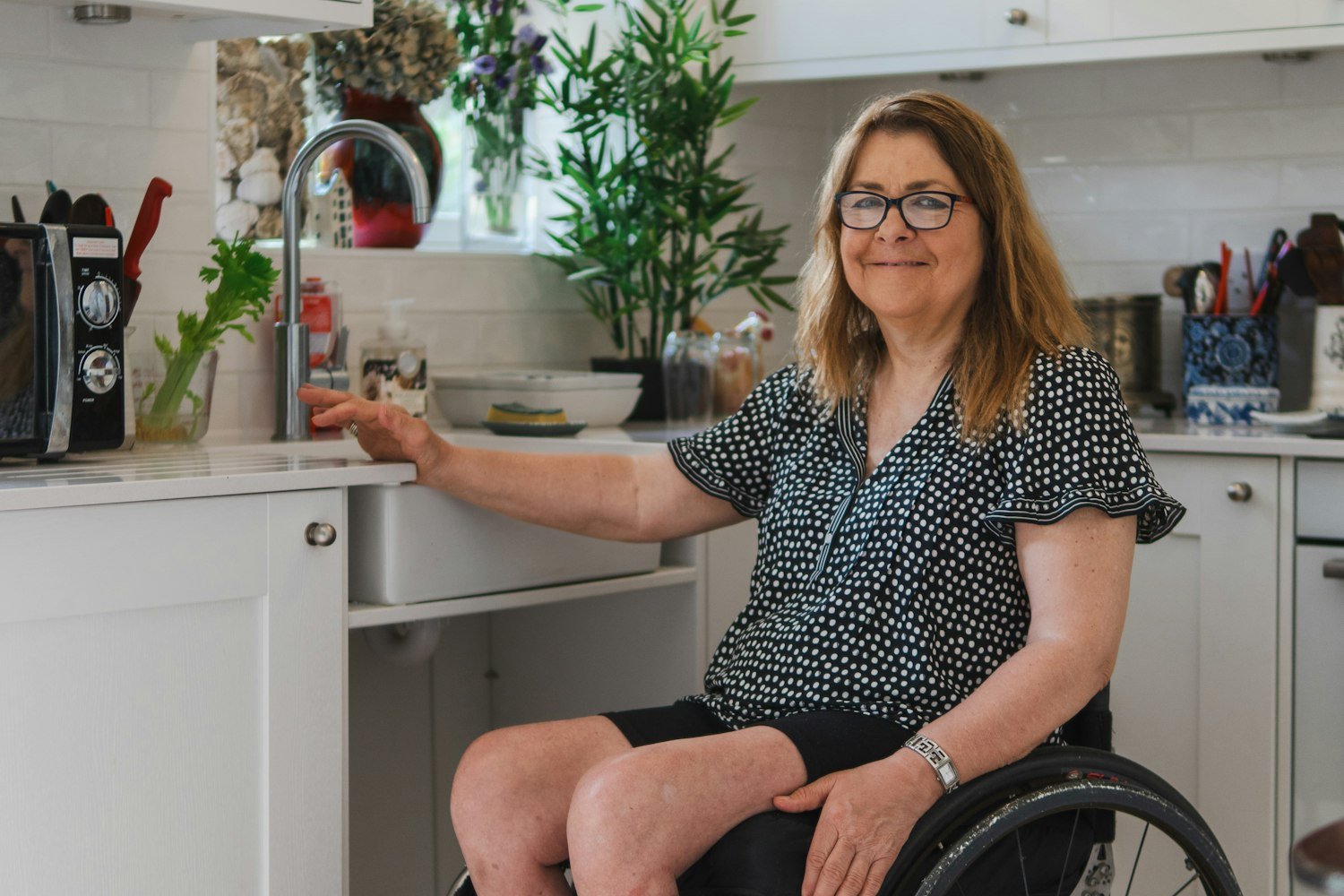 Woman using a wheelchair at an accessible kitchen sink at home, NDIS in home support